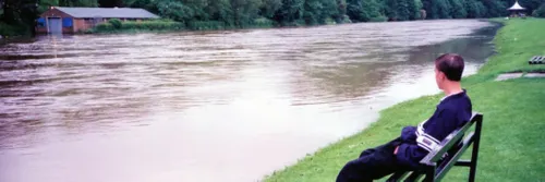一名男子坐在洪水泛滥的威尔河旁的长凳上