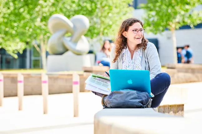 Student sat studying and smiling on campus