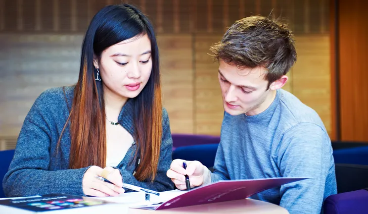 Two students working together over open academic textbooks