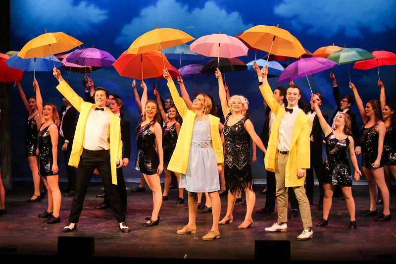 Performers posing on stage in raincoats holding umbrellas