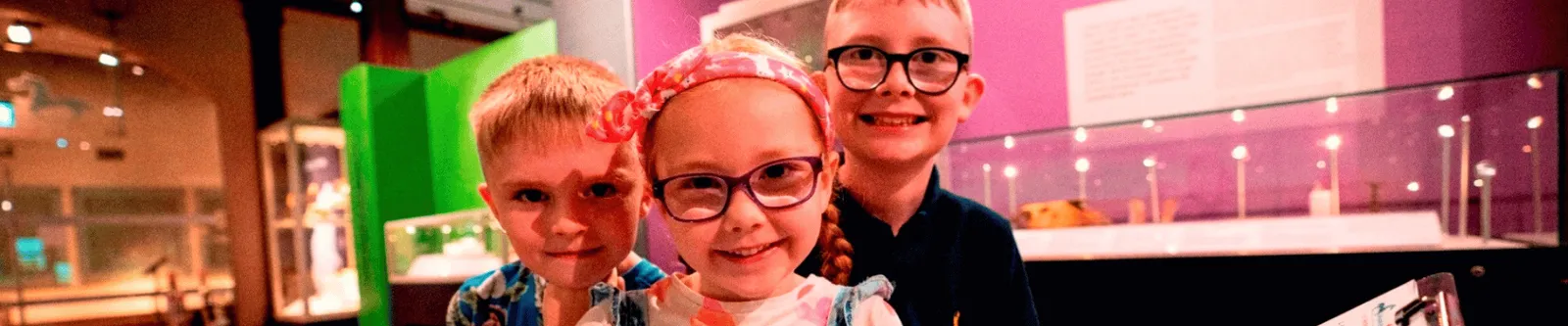 Three children sat in a gallery within the Museum of Archaeology