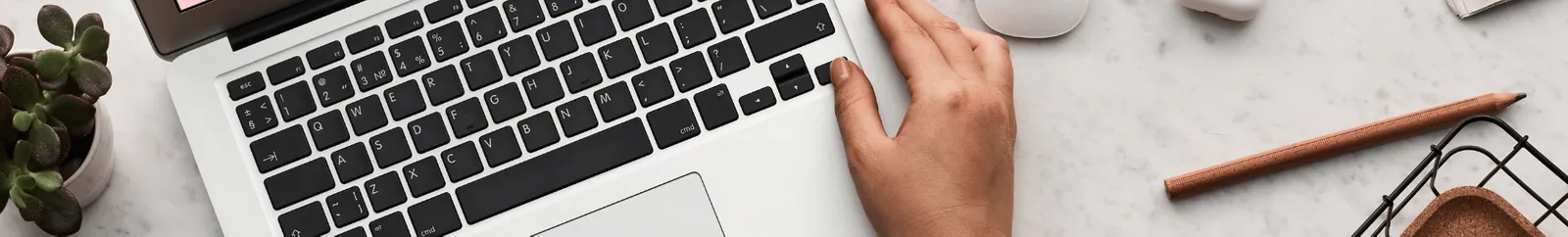 hands on a laptop keyboard with a plant, pencil and basket in view.