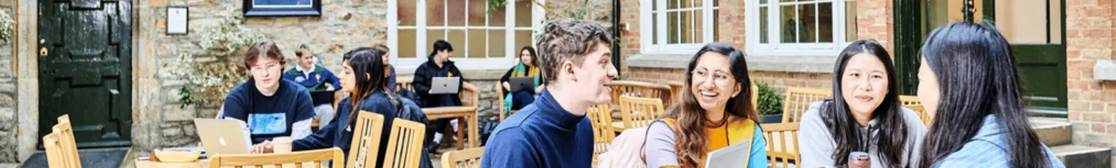 A group of students outside chatting around a table with laptops