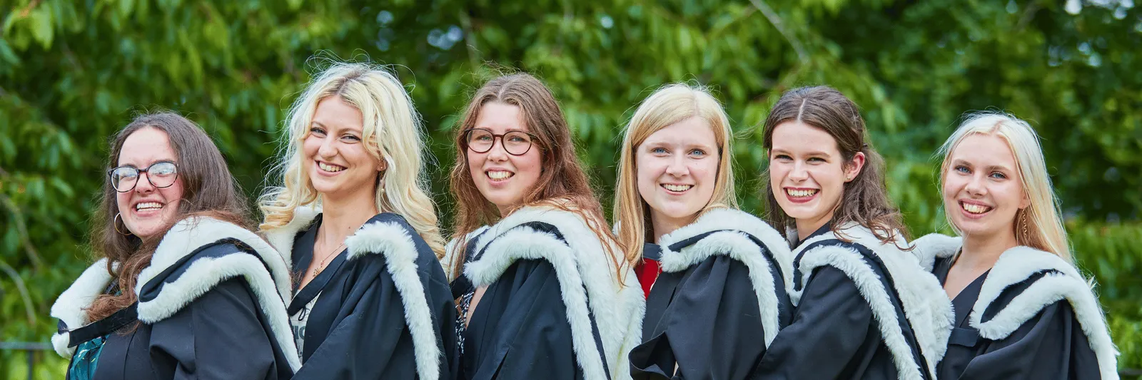 A group of students in gowns smiling standing behind one another