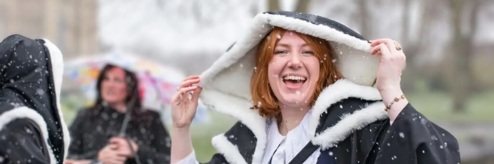 A student holding the hood of a graduation gown with flurries of snow