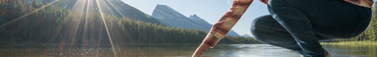 A river with mountains and a woman placing her hand in the water