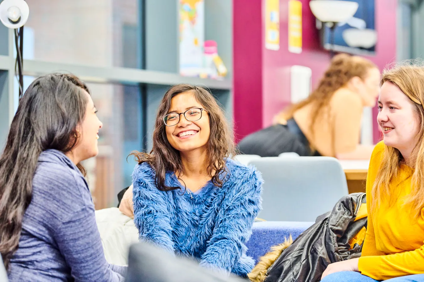A group of female post-graduates sit together chatting and laughing. The space is brightly lit and colourful.