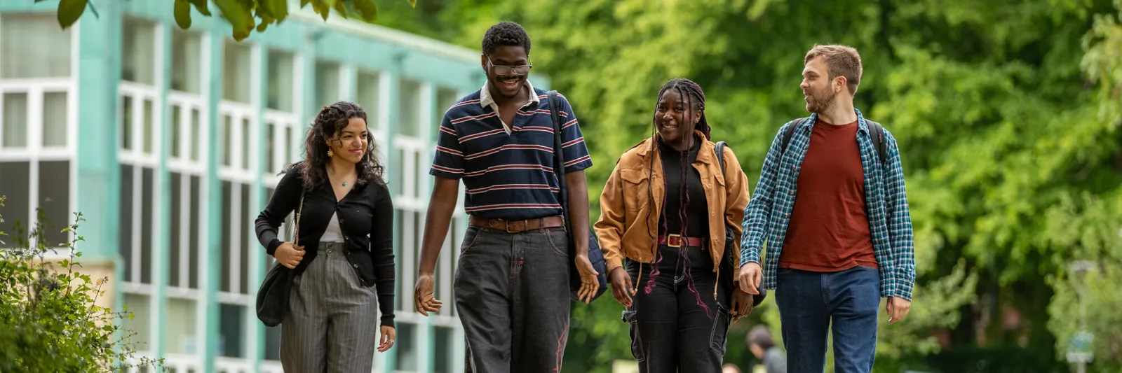 A group of four students walking together. They are talking to each other and smiling.