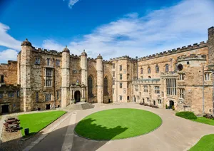 High stone buildings on two sides of a courtyard with a circular lawn in the centre and smaller areas of lawn against the sides.