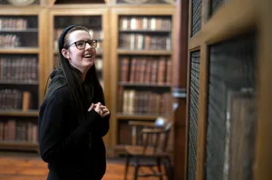 A student smiles as they look at the bookshelves in the historic library