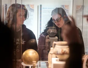 Image of two students looking into a museum case discussing the objects they are looking at on display