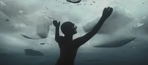 A diver under a sheet of ice reaches for the surface.