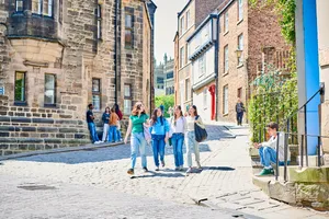 A group of students walking down a cobbled street lined with old stone buildings, with a glimpse of Durham Cathedral in the background