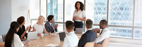 Businesswoman stands to address meeting around board table