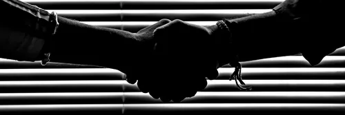 monochrome photo of people shaking hands in front of a horizontal blind