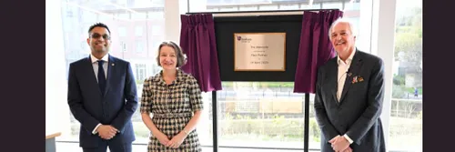 Three people standing in front of a plaque, revealed by a pulled curtain