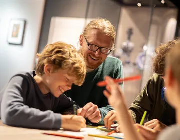 A parent and child are sat smiling whilst colouring in a craft activity in the Silk Roads Gallery of the Oriental Museum