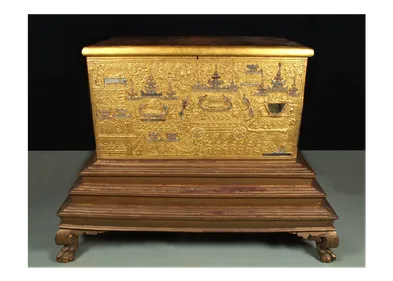 A Buddhist manuscript chest with intricate gold decoration on a stepped plinth.