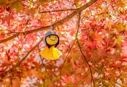 Yellow Japanese Weather Doll for rain hanging from a maple tree