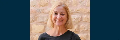 Professor Anna Leone is stood in front of a light coloured stone wall smiling to the camera.