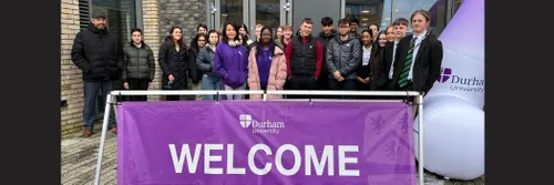 Young people standing against a building, behind a purple  'welcome' banner