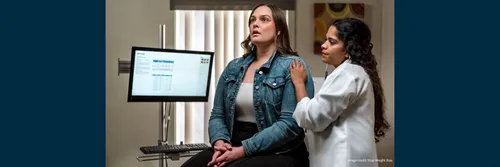 Patient sat in medical consultation with healthcare practitioner to their left listening with a stethoscope