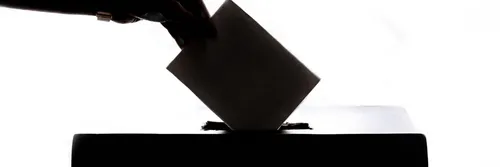 Silhouette of a hand putting a voting slip into a box