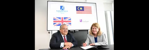 A man and a woman sitting at a desk, signing a document, smiling at the camera.