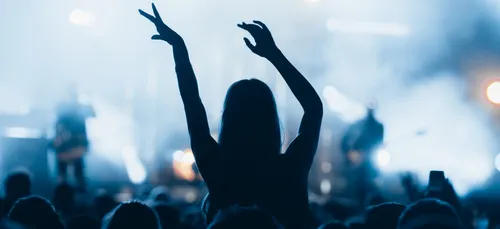 Silhouette of a woman in a crowd cheering on a music band