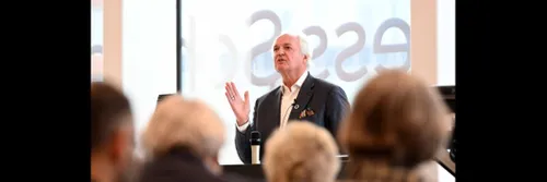 Man speaking to audience, backs of heads in foreground