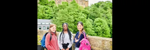 Three female students standing on a bridge, with Castle in background