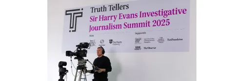 A video camera operator, with camera, stood in front of a large sign for the Truth Tellers summit