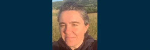 A head and shoulders close up photograph of Professor Sarah Semple. Sarah is smiling at the camera while standing in a field surrounded by countryside.