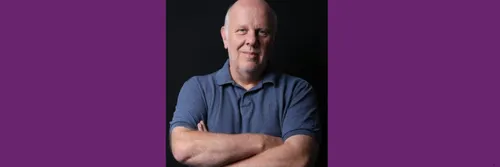 Professor Stephen Gorard standing with his arms crossed against a black background