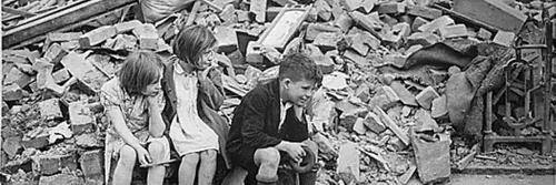 Black and white photograph of children sitting amongst rubble after bombing raids on London in WW2