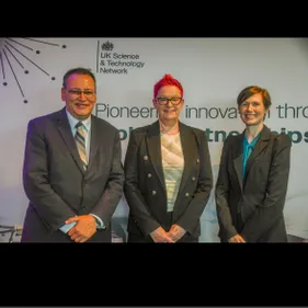 A male and two females in suits stood in a line smiling for a formal photograph