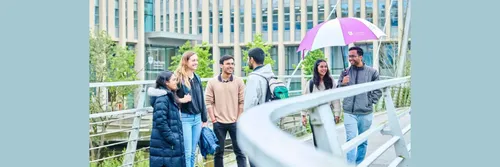 A group of students standing on a bridge talking and smiling