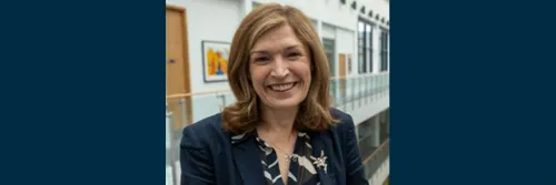 Head and shoulders picture of Amanda Wilcox smiling and looking at the camera. She is standing in front of an office background.