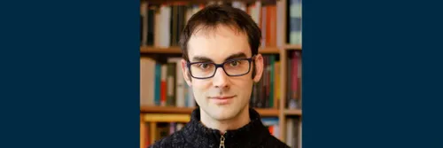 A man wearing glasses and blue woolen zip up jumper smiling at the camera