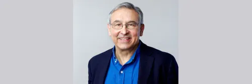 Professor Carlos Frenk in light blue shirt and dark blue jacket smiles at the camera