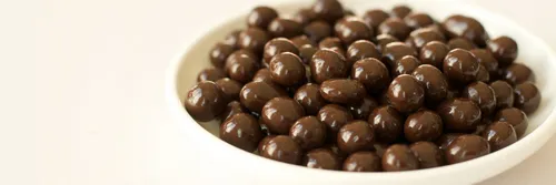 A white bowl containing chocolate balls with a plain background