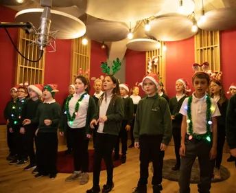 A group of children singing in the recording studio at Collingwood, wearing Christmas accessories