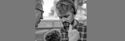 A black and white image of David Knowles holding a microphone looking towards the ground
