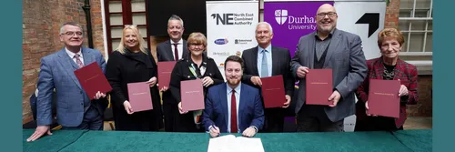 Leaders of seven North East councils stand behind Levelling Up Minister Jacob Young who is sitting at a table signing a document