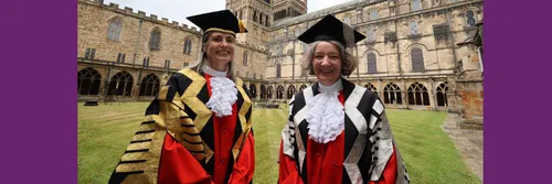 Dr Fiona Hill and Karen O'Brien stood together smiling wearing academic gowns with Durham Cathedral in the background