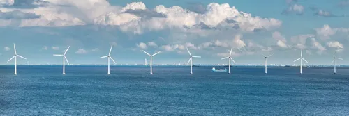 Large white wind turbines in the sea under a blue sky with fluffy white clouds