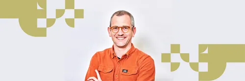 James Rowlands wearing an orange top smiling with his arms folded