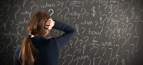 Woman looking at a blackboard with question marks on it.