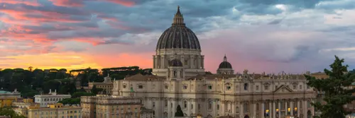 The dome of St Peter's Basilica in Rome against an orange and blue dusk sky