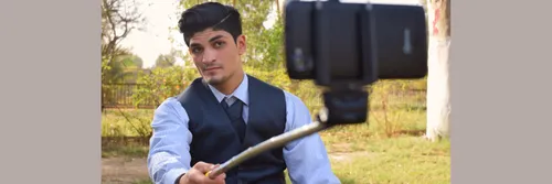 A man wearing a smart blue shirt and waistcoat poses for a selfie using a selfie stick